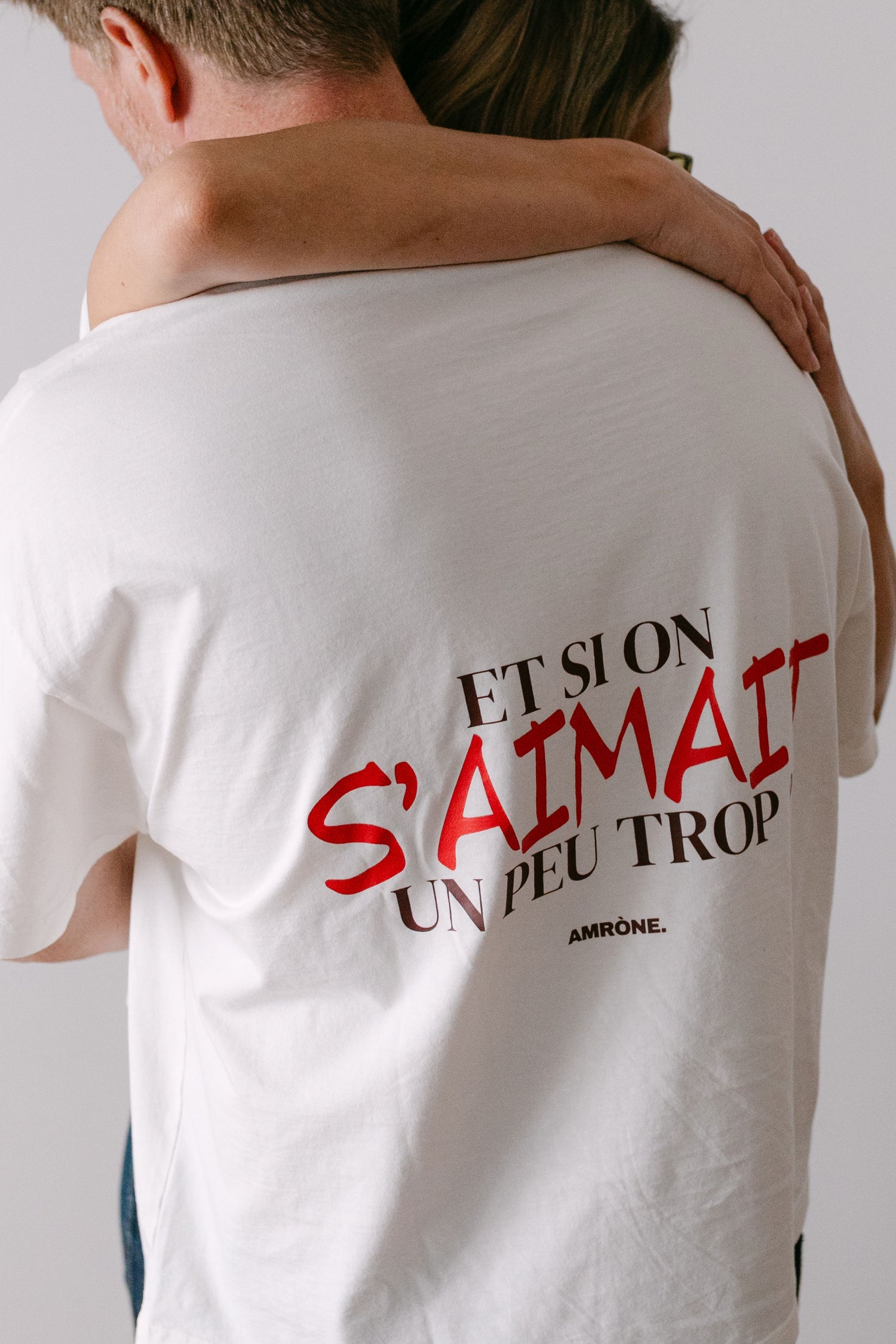 Couple qui s'enlace. L'homme porte un Tee shirt blanc oversize "et si on s'aimait un peu trop?" unisexe de la marque Amrone.
