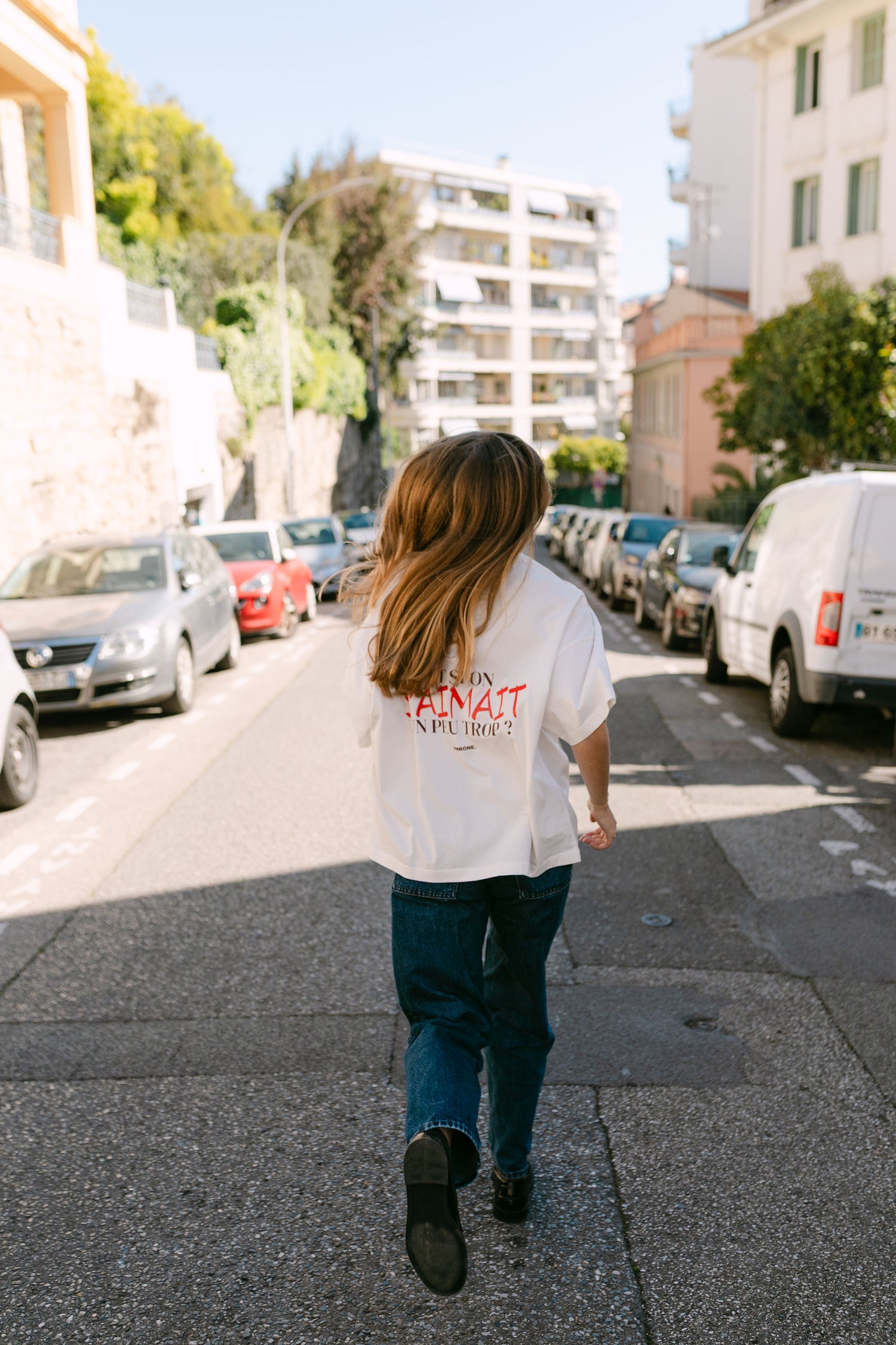 Femme qui court dans la rue avec son Tee shirt blanc oversize "et si on s'aimait un peu trop?" unisexe de la marque Amrone.